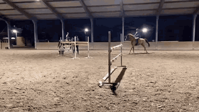a horse is jumping over a hurdle in a indoor arena .