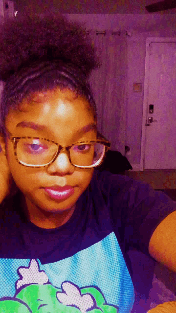 a girl wearing glasses and a t-shirt with a frog on it takes a selfie