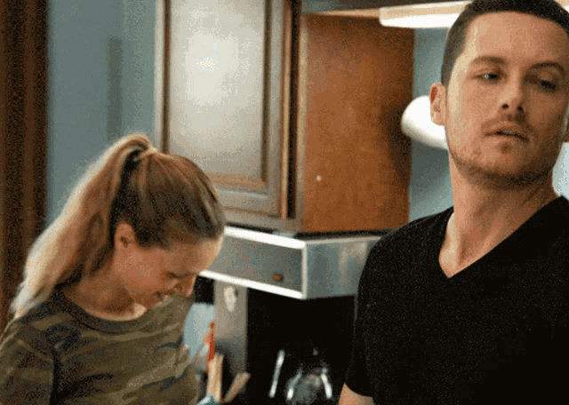 a man in a black shirt stands next to a woman in a ponytail in a kitchen