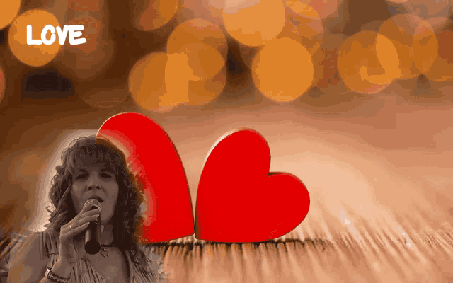 a woman singing into a microphone in front of two red hearts and the word love