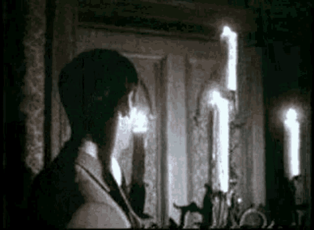 a man in a suit is standing in a dark room with candles in the background .