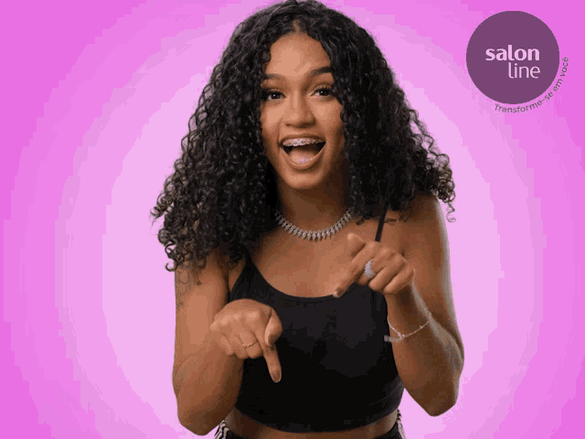 a woman with curly hair pointing at the camera with a salon line logo in the background