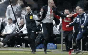 a man in a suit and red tie is running on a soccer field
