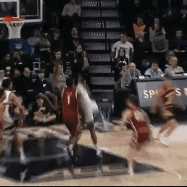 a group of basketball players are playing a game of basketball on a court with a crowd watching .