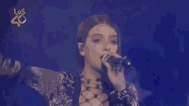 a woman is singing into a microphone on a stage with her hand in the air .
