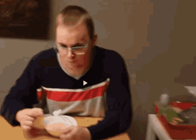a man wearing glasses is sitting at a table eating a meal