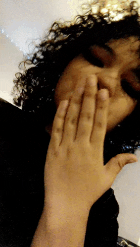 a woman with curly hair covering her face with her hands