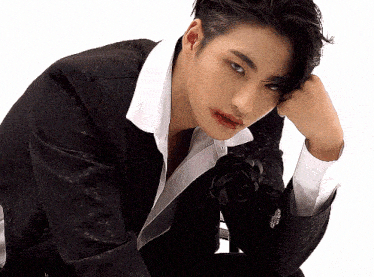 a young man in a black suit and white shirt is sitting down