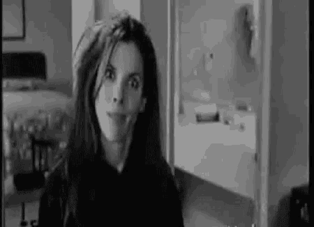 a black and white photo of a woman looking at the camera in a room .