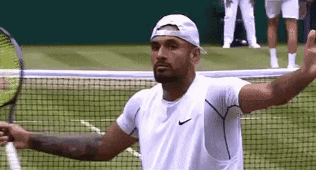 a man is holding a tennis racquet on a tennis court while wearing a hat .