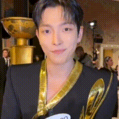 a man wearing a black jacket and a gold ribbon around his neck is holding a trophy .