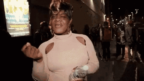 a woman is standing on a sidewalk holding a bottle of water and making a funny face .