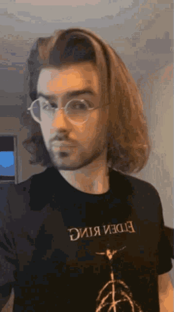 a man with long hair wearing glasses and a black shirt that says eden king
