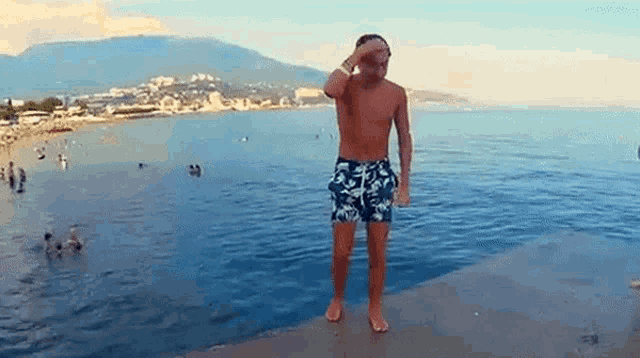a shirtless man in blue shorts is standing on a ledge overlooking the ocean .