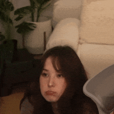 a woman is sitting on a couch in a living room with a plant in the background .