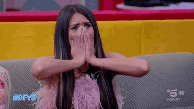a woman in a pink feathered dress is sitting on a couch and covering her face