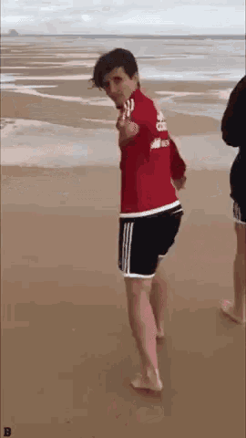 a man in a red shirt and black shorts is dancing on a beach