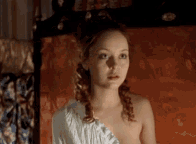 a woman without a shirt is standing in front of an orange bed
