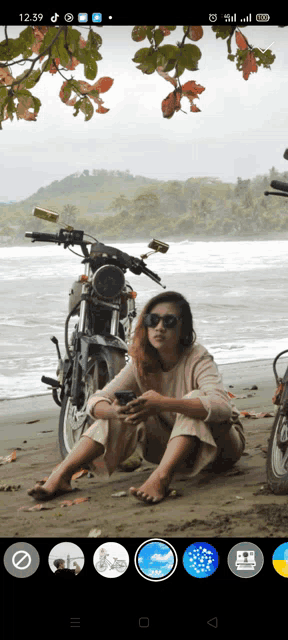 a woman sits on a beach next to a motorcycle