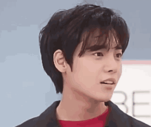 a young man with short hair is wearing a black jacket and a red sweater .