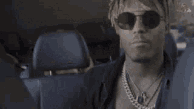 a man wearing sunglasses and a necklace is sitting in the back of a car .