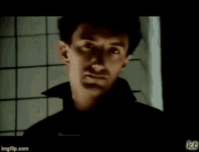 a man in a black coat is standing in front of a tiled wall in a dark room .