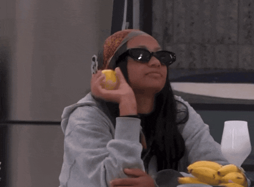 a woman wearing sunglasses and a bandana is holding a banana