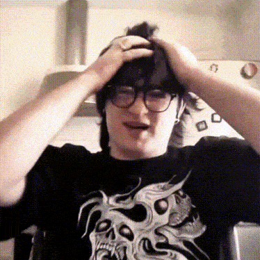 a man wearing glasses and a black shirt with a skull on it is holding his head