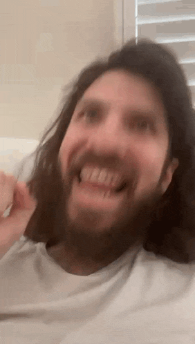 a man with long hair and a beard is laying on a bed and smiling .