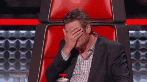a man in a suit is covering his face while sitting in a red chair .