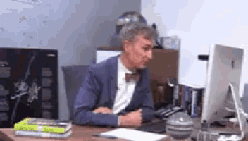a man in a suit and bow tie is sitting at a desk with a computer .