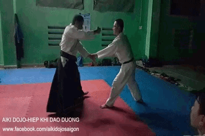 two men are practicing martial arts in a gym with the website facebook.com/aikidoosaigon on the bottom of the screen .