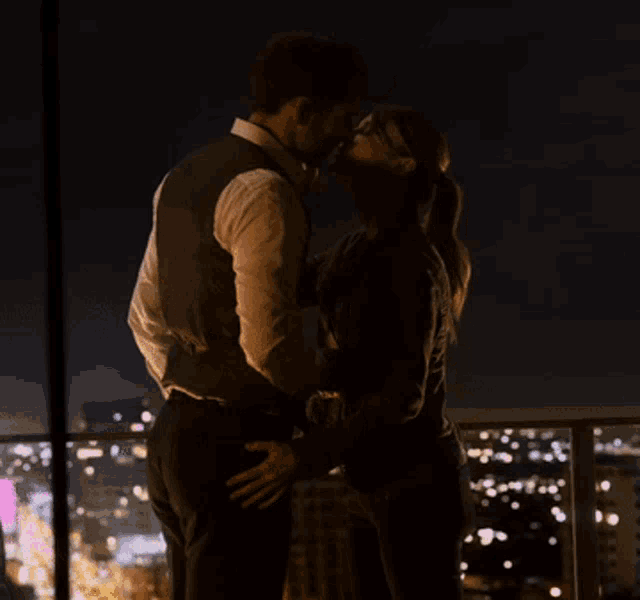 a man and a woman are kissing in front of a city at night