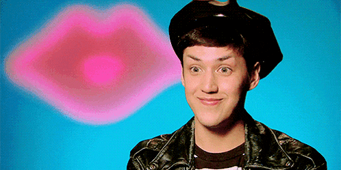 a young man wearing a hat and a leather jacket is smiling in front of a pink lip