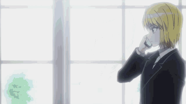 a man in a suit is talking on a cell phone in front of a window