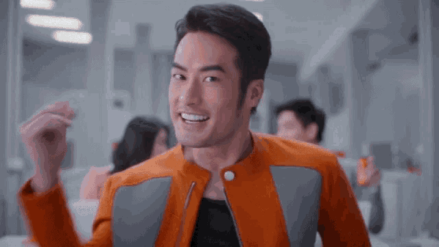 a man in an orange jacket is smiling and holding a drink in his hand .