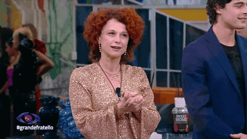 a woman with red hair applauds in front of a sign that says grandefratello