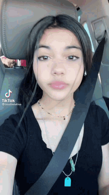 a young girl is sitting in a car wearing a seat belt and a necklace .