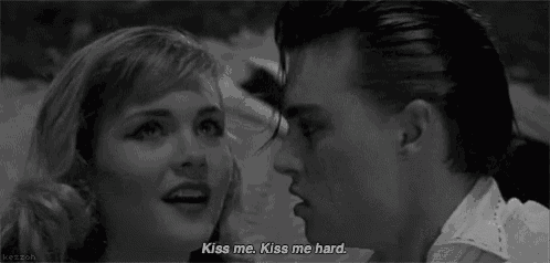 a man and a woman are kissing in a black and white photo with the man saying kiss me kiss me hard .