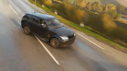 a black suv is driving down a road with trees in the background .