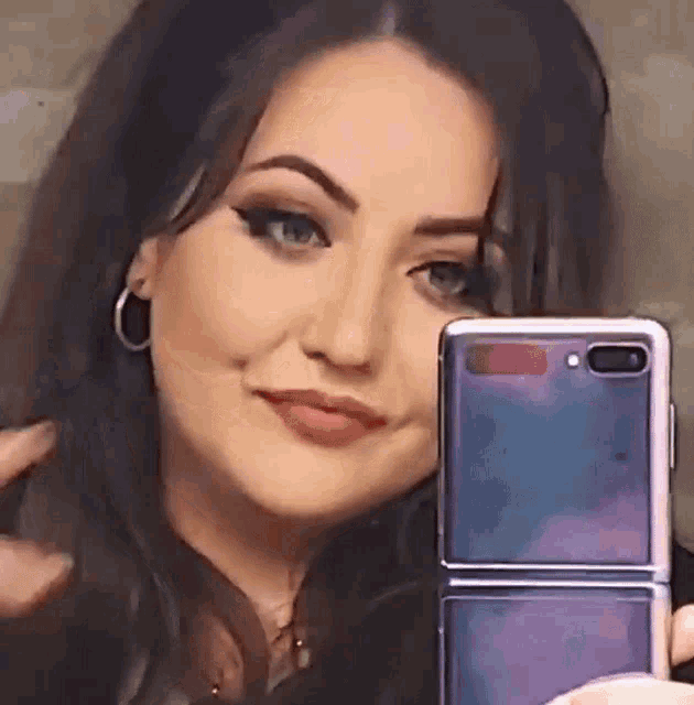 a woman is taking a selfie with her phone in front of her face .