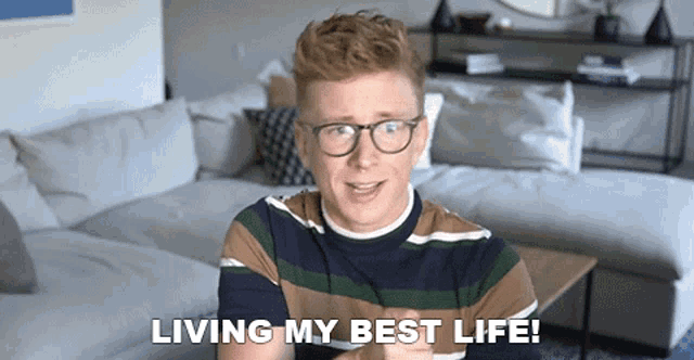 a man with glasses is sitting on a couch and saying living my best life .