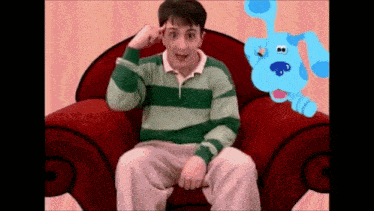 a man is sitting in a chair with a blue dog behind him .