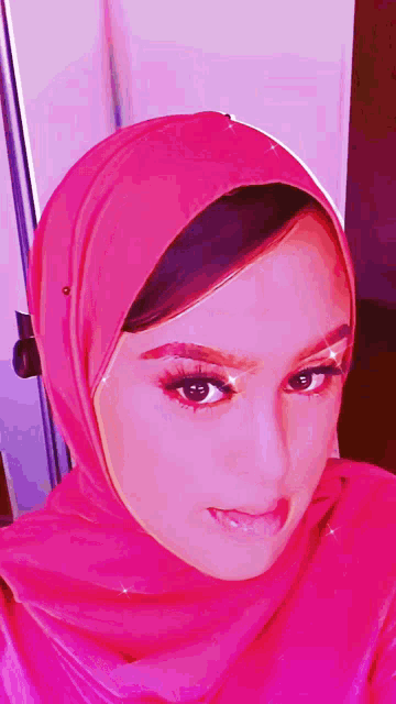 a woman wearing a pink hijab is smiling and looking at the camera