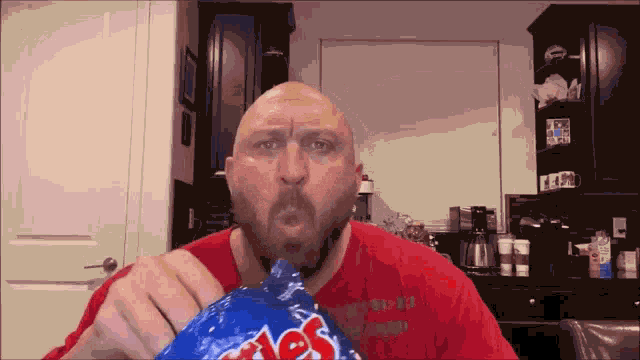 a bald man in a red shirt is holding a bag of coles