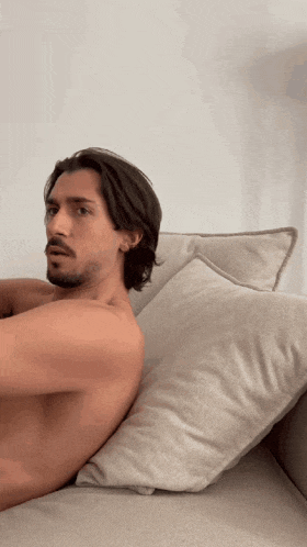 a shirtless man with a beard is laying on a couch