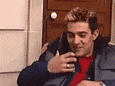 a man in a red shirt is talking on a cell phone .