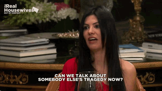 a woman is sitting at a table with a glass of wine and says can we talk about somebody else 's tragedy