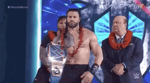 roman reigns is wearing a lei and holding a wrestling championship belt while standing on a stage .