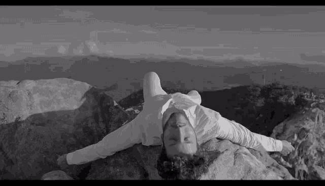 a black and white photo of a man laying on top of a rocky mountain .